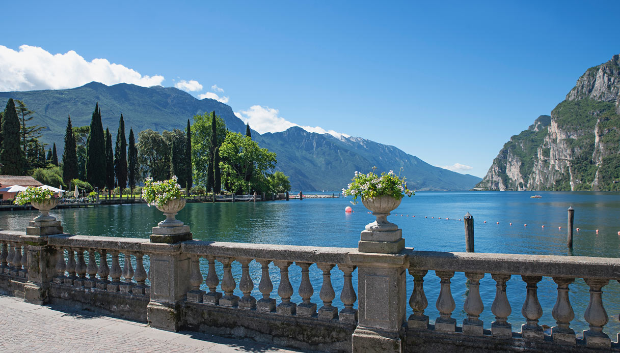 View of Lake Garda from a stone balustrade with cypress trees, blue water and mountains
